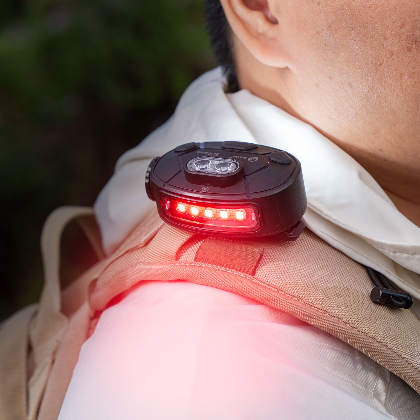 Red LED light attached to a backpack on a person's shoulder with a blurred natural background